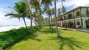 Un hotel frente a la playa con piscina, palmeras y vistas al océano.