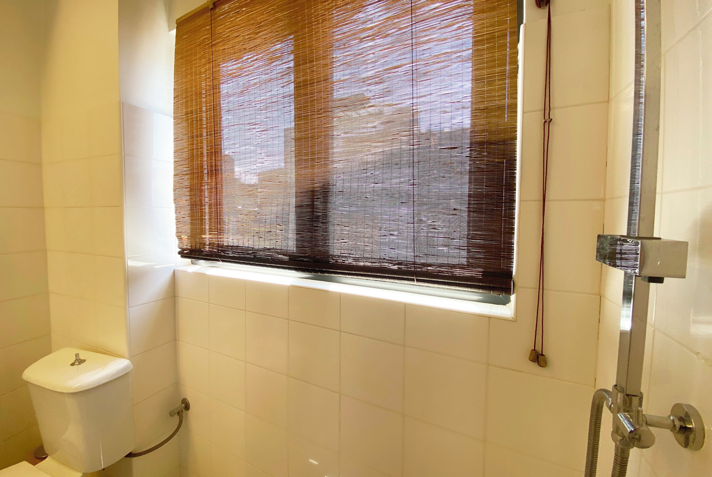 Ein Badezimmer mit Toilette, Dusche und einem Fenster mit Jalousien.