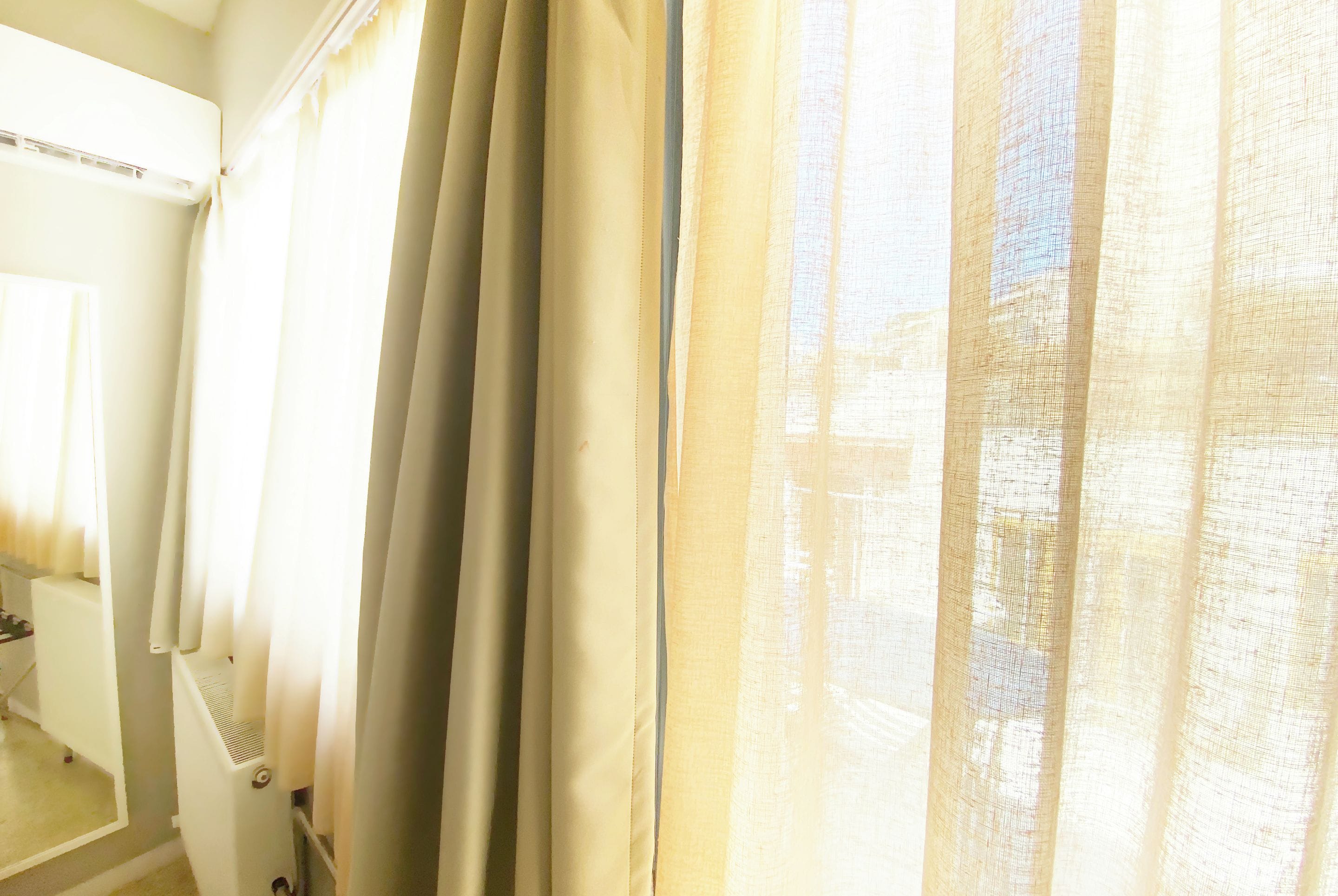 A room with a window covered by sheer curtains, a white radiator, and a door leading to another room.