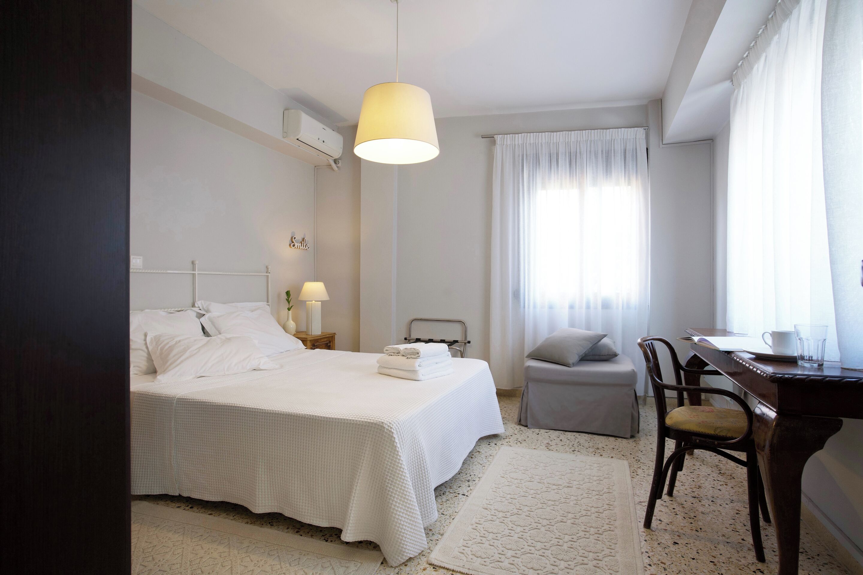 A hotel room with a bed, a desk, a chair, a lamp, and a window with curtains.