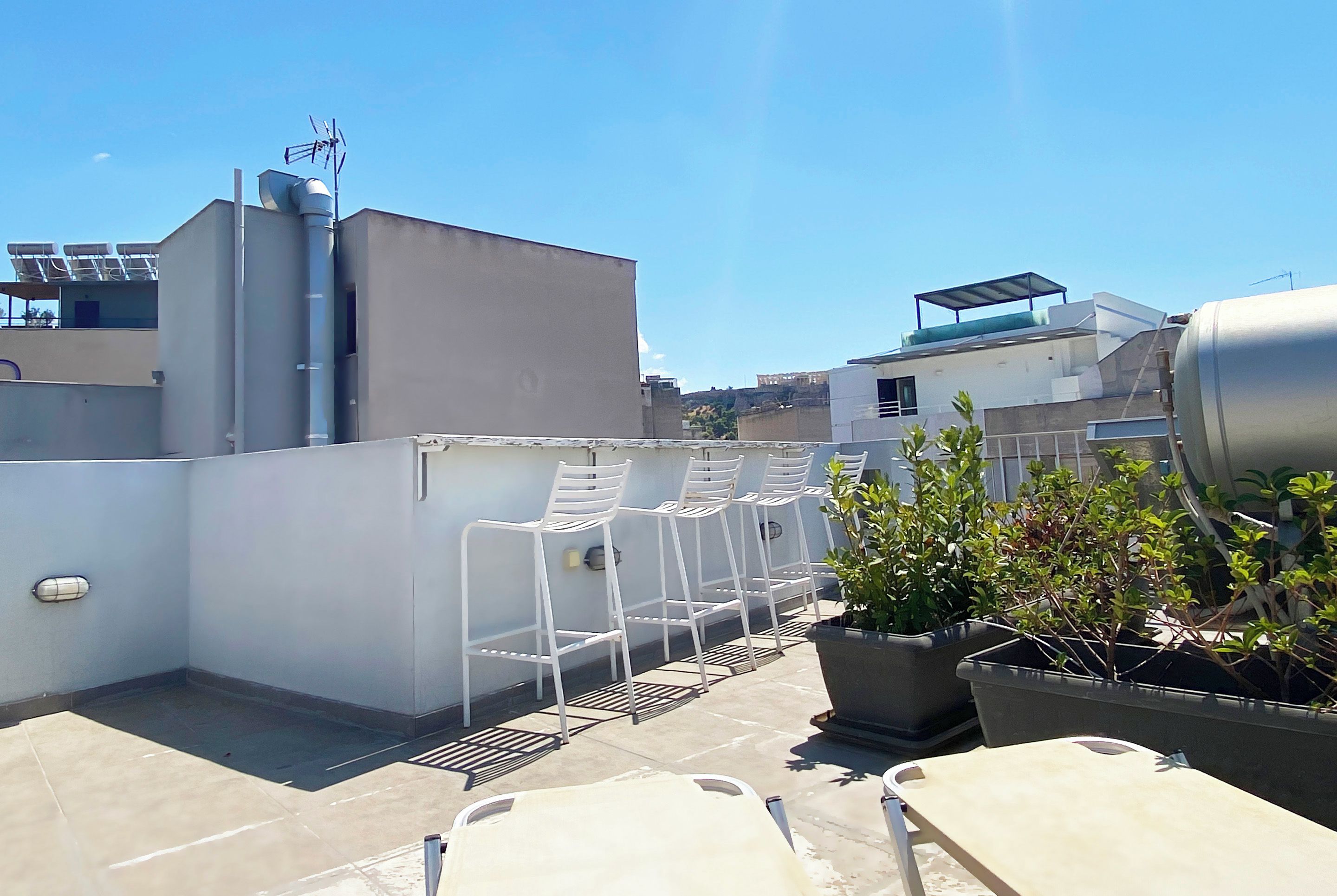 A rooftop terrace with white metal chairs, a potted plant, and a water tank.