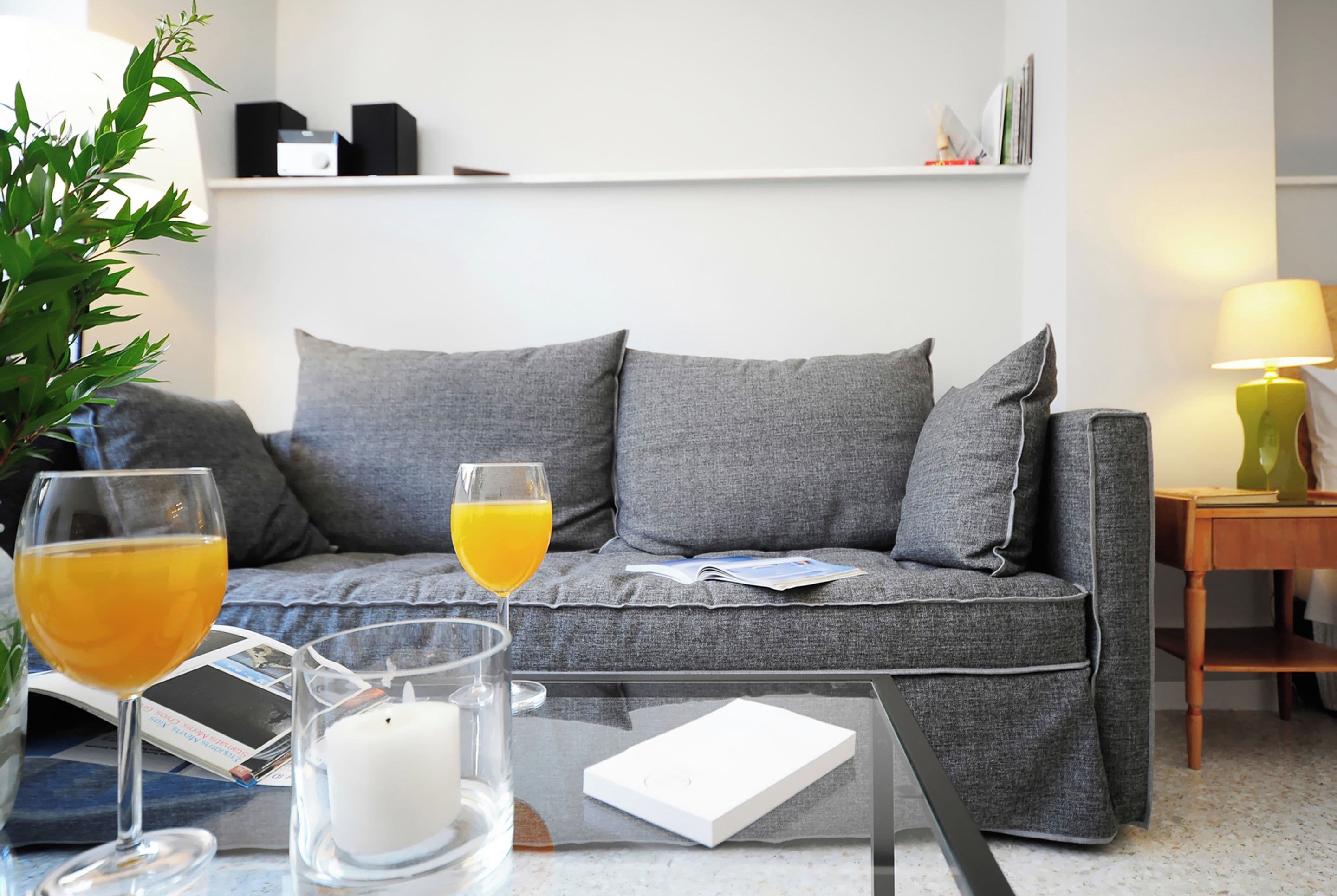 A modern living room with a grey sofa, a glass coffee table, and a small side table with a lamp.
