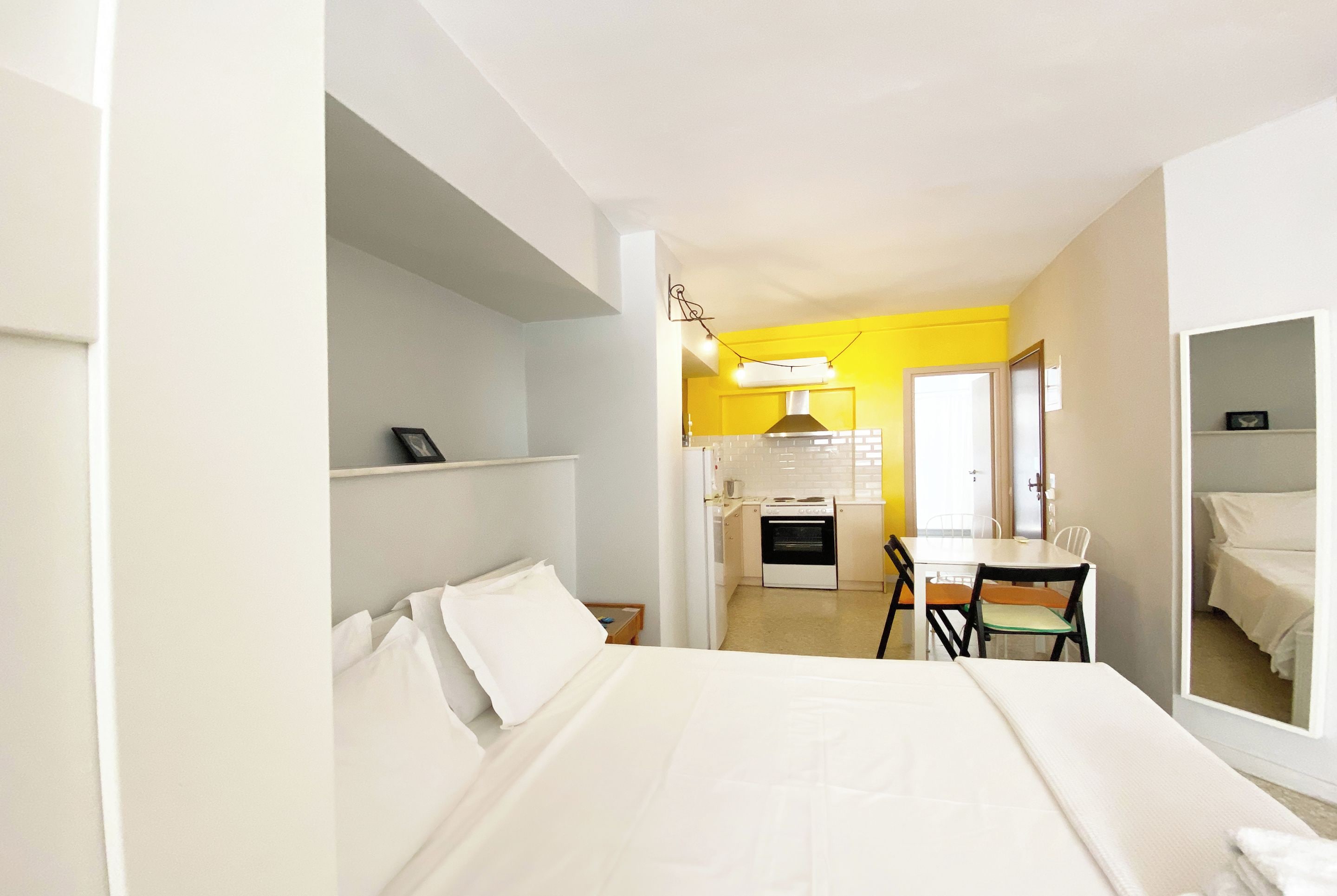 A hotel room with a bed, a small kitchenette, a dining table with chairs, and a mirror.