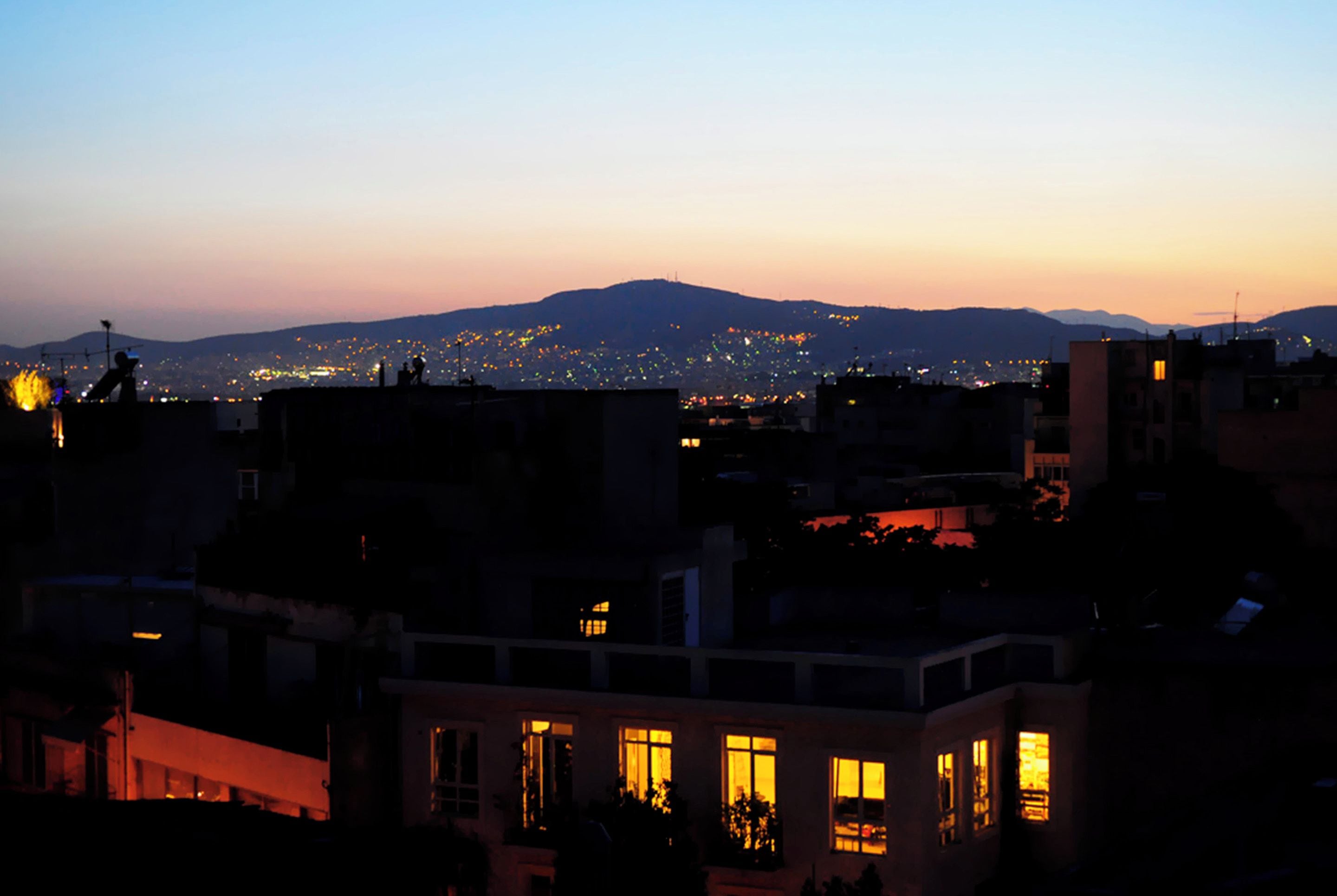 Une vue d’une ville au crépuscule, avec des bâtiments et une montagne en arrière-plan.