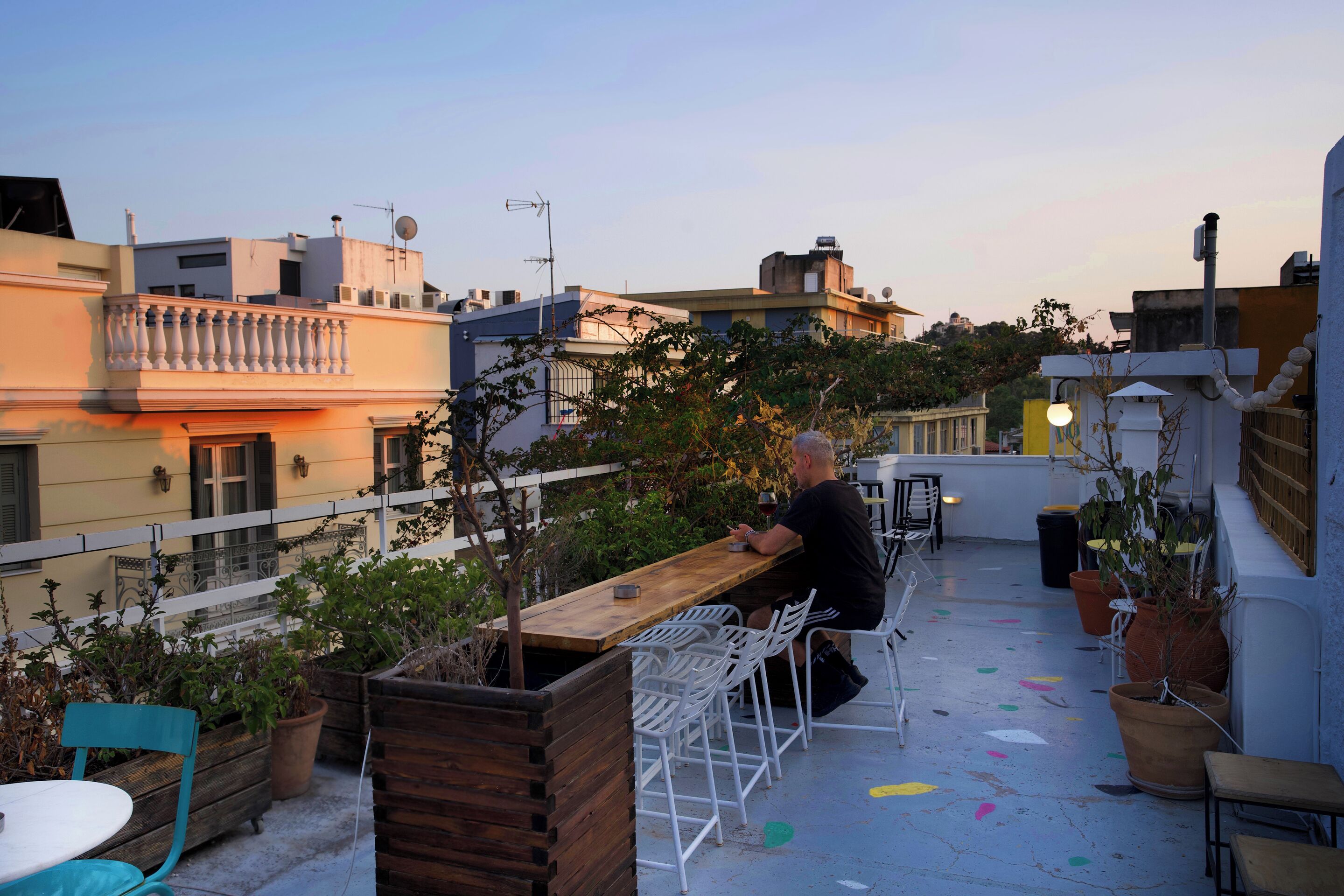 Une terrasse sur le toit, avec une table et des chaises en bois, entourée de plantes en pot et d’une clôture blanche.