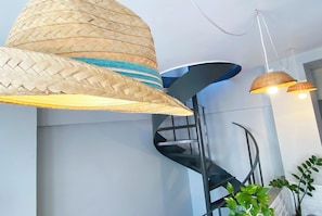 Un interior modern amb una escala de caragol, llums de fibres naturals i una planta en test.