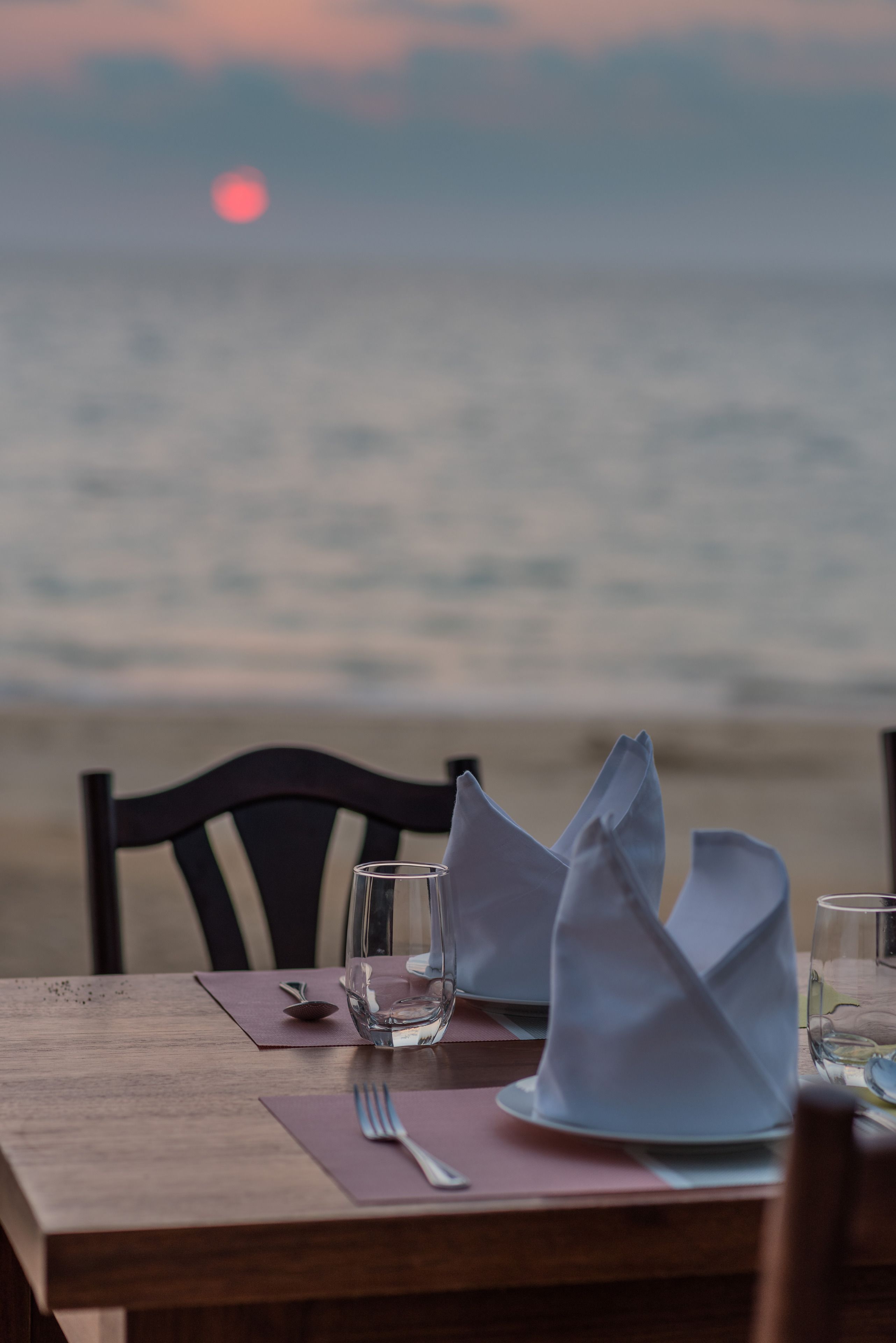 A table set for dining with a view of the ocean and a sunset in the background.