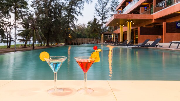 A poolside view with two cocktails and a building with balconies in the background.