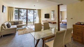 A modern hotel room with a glass dining table, a sofa, a TV, and a bed.