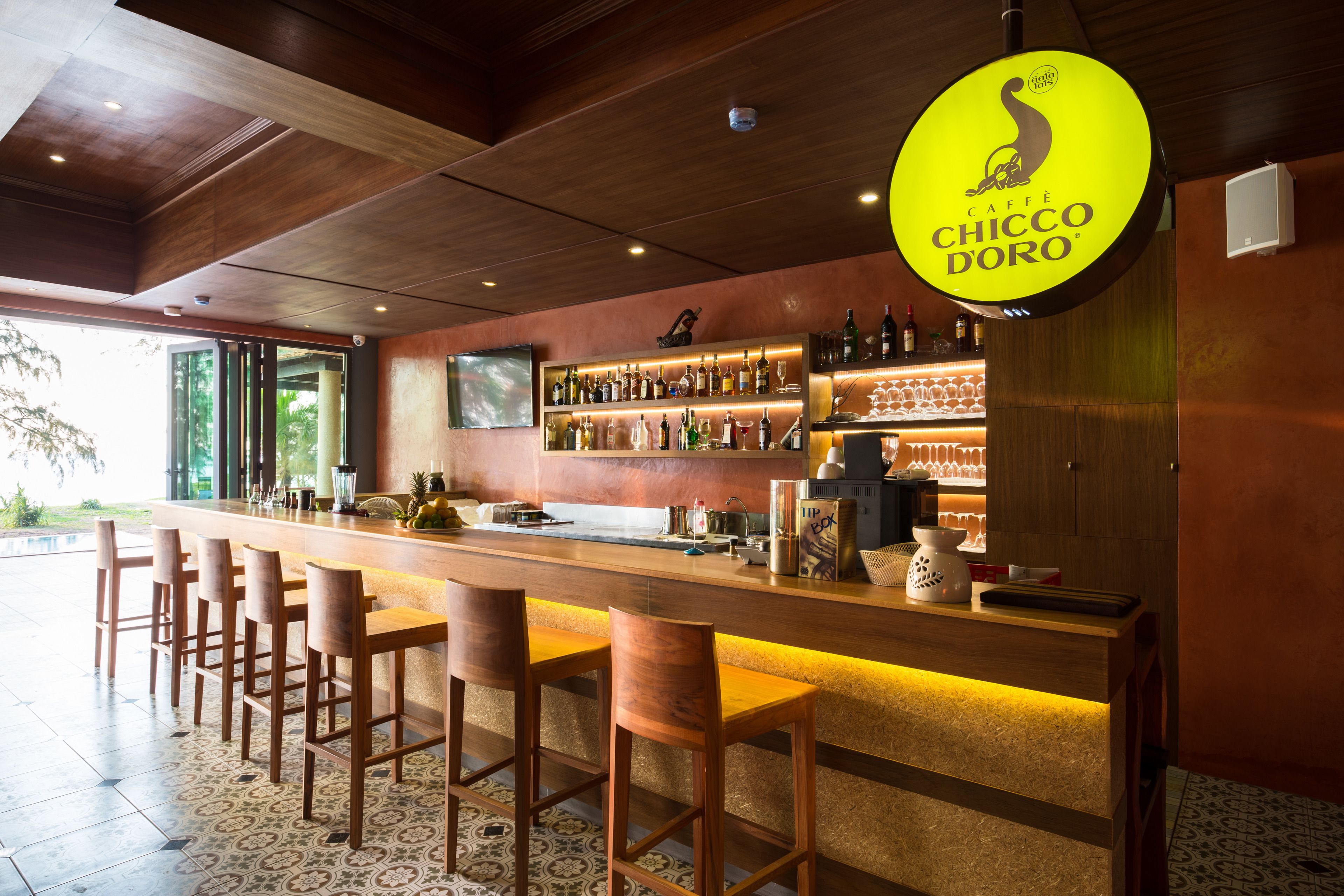 A bar area with a long counter, multiple stools, and a variety of bottles and glasses.
