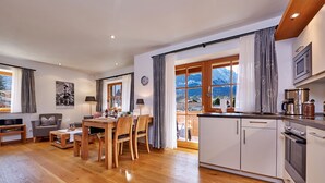 Una cocina moderna con armarios de madera, un comedor con mesa y sillas, y vistas a montañas a través de amplios ventanales.