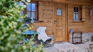 Una cabaña de madera con base de piedra, una mesa azul con una butaca de piel blanca y una cruz en la pared.