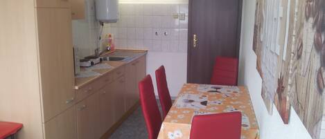 A compact kitchen with a sink, cabinets, and a water dispenser. There is a dining table with red chairs and a floral tablecloth.