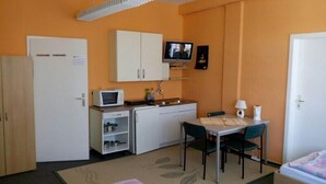 A compact room with a kitchenette, a dining area with two chairs, a bed, and a television mounted on the wall.