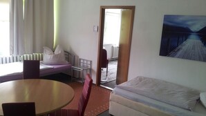 A hotel room with a bed, a small table, a chair, a sofa, and a painting on the wall.