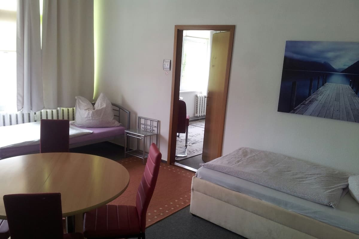 A hotel room with a bed, a small table, a chair, a sofa, and a painting on the wall.