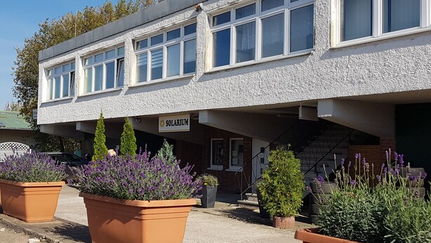 A building with a sign reading "SOLARIUM" and multiple windows. There are potted plants in front of the building.