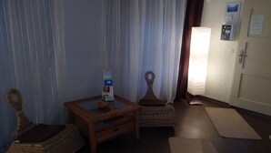 A room with a wicker chair, a small wooden table, a standing lamp, and a door with a control panel.