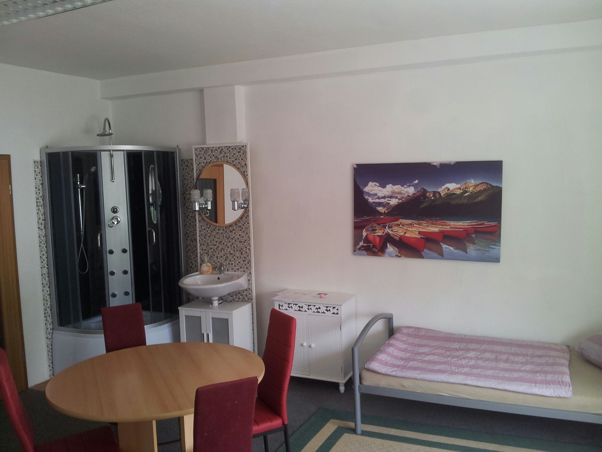 Habitación con ducha, lavamanos y un cuadro de un paisaje montañoso.