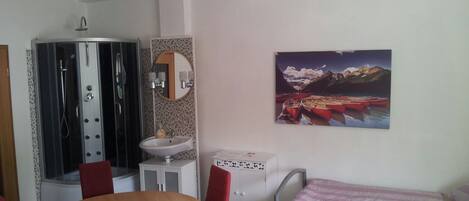 Habitación con ducha, lavamanos y un cuadro de un paisaje montañoso.