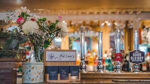 Eine Barbereich mit einem Schild 'Pub Lover's Geschenk', verschiedenen Zapfhähnen und einer Blumenkomposition.