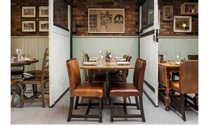 A dining area with wooden tables and chairs, framed pictures on the wall, and a brick wall.