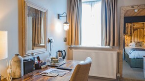 A room with a wooden table, a mirror, a lamp, and a view of a bed with a window.