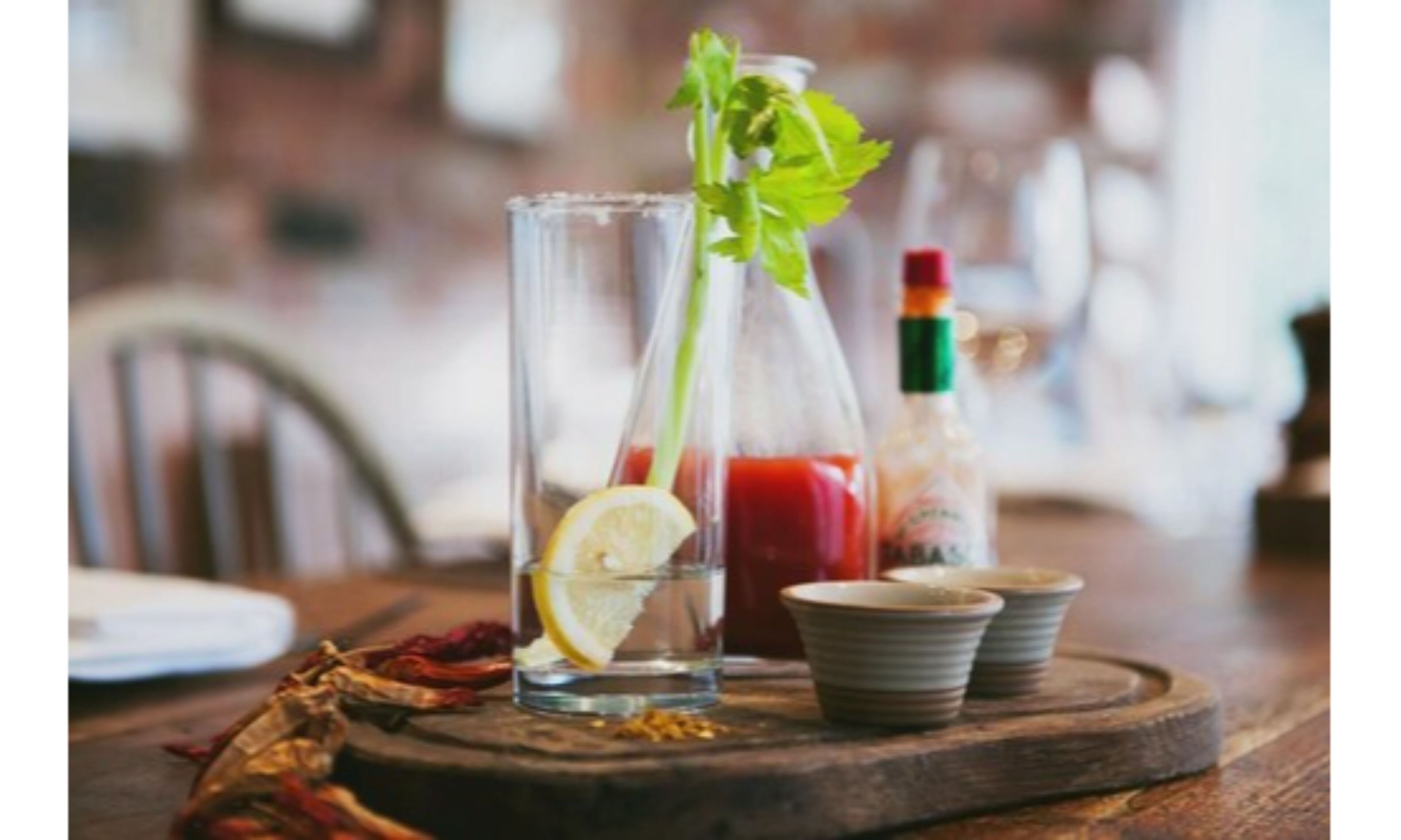 A glass with a lemon slice and a sprig of parsley, a bottle of ketchup, and two small bowls on a wooden board.