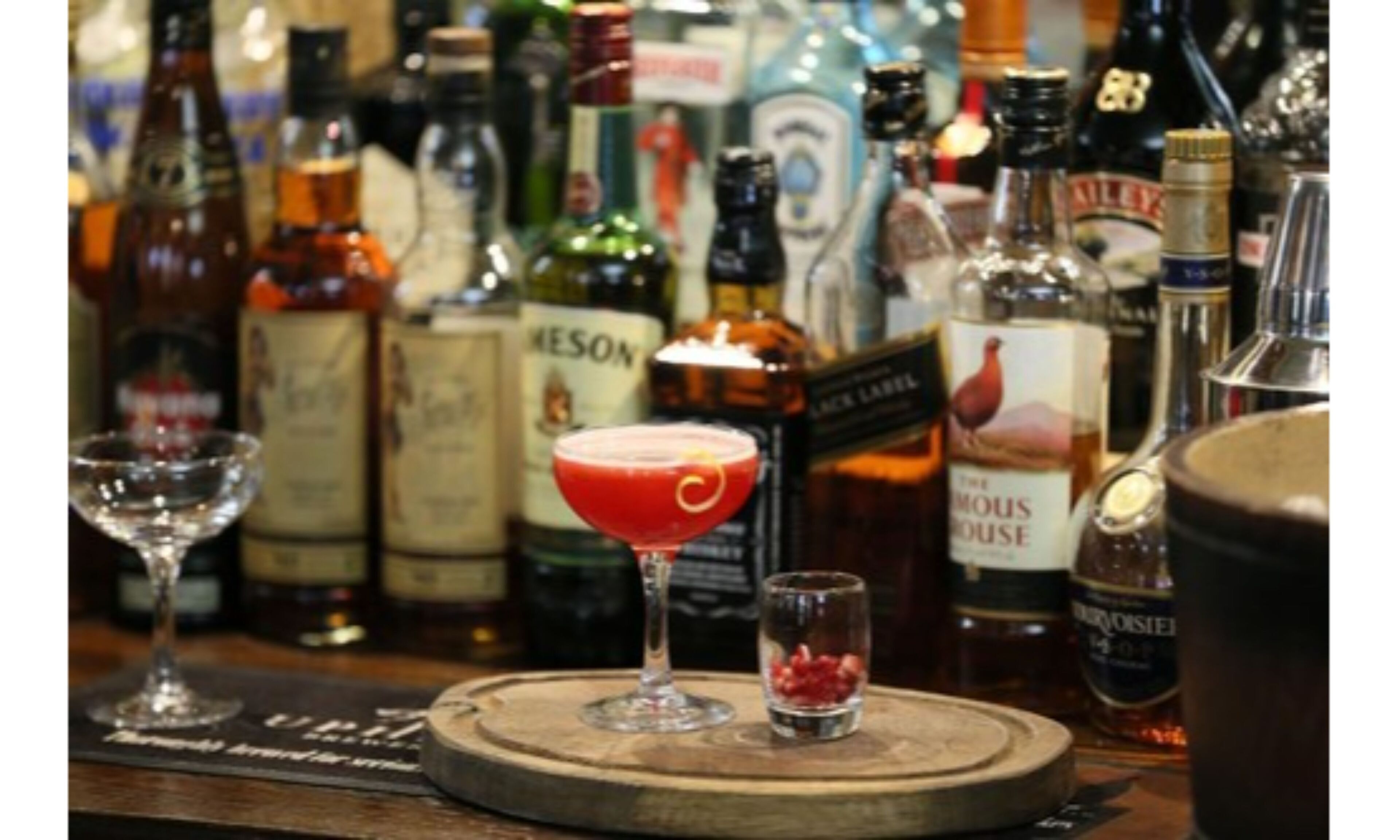 A bar area with various bottles of alcohol and a martini glass on a wooden coaster.