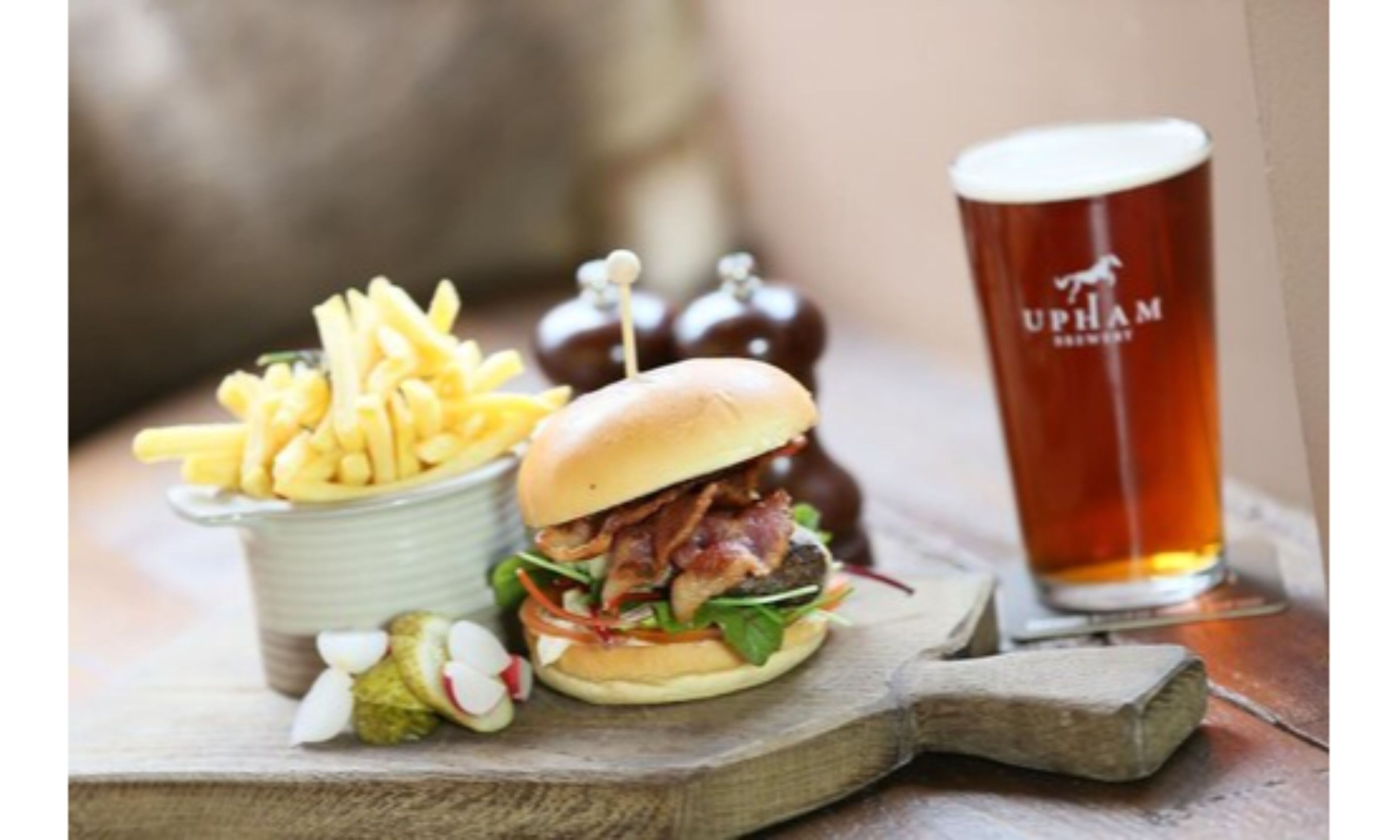 Una comida con una hamburguesa, papas fritas y una cerveza en una tabla de madera.
