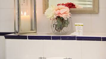 Une salle de bain avec un lavabo blanc, un miroir, une bougie et un vase rempli de fleurs.