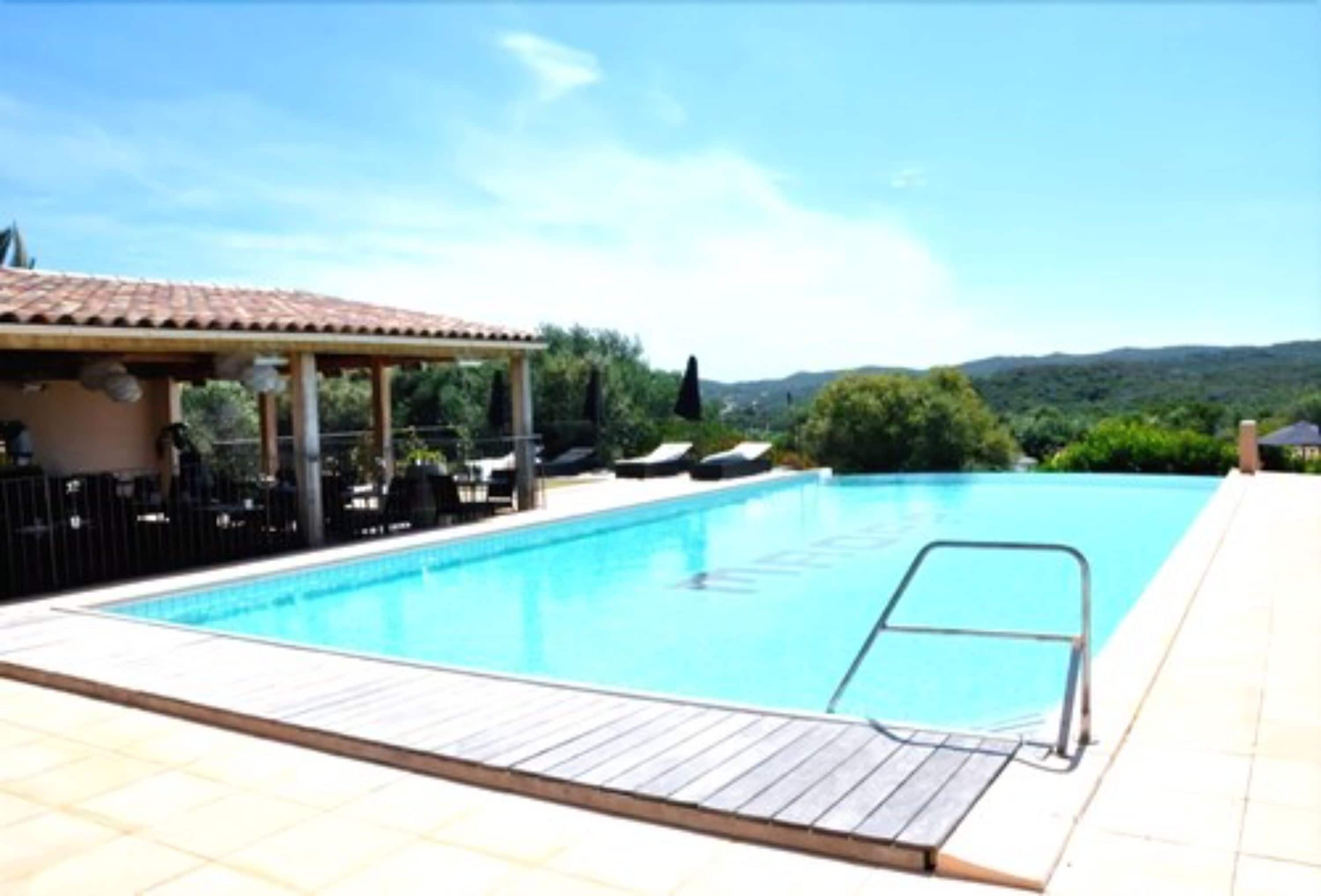 A swimming pool with a wooden deck, lounge chairs, and a covered seating area.