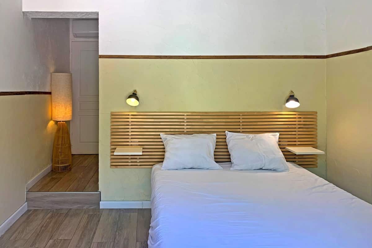 A bedroom with a wooden headboard, two bedside lamps, a bed with white bedding, and a nightstand.