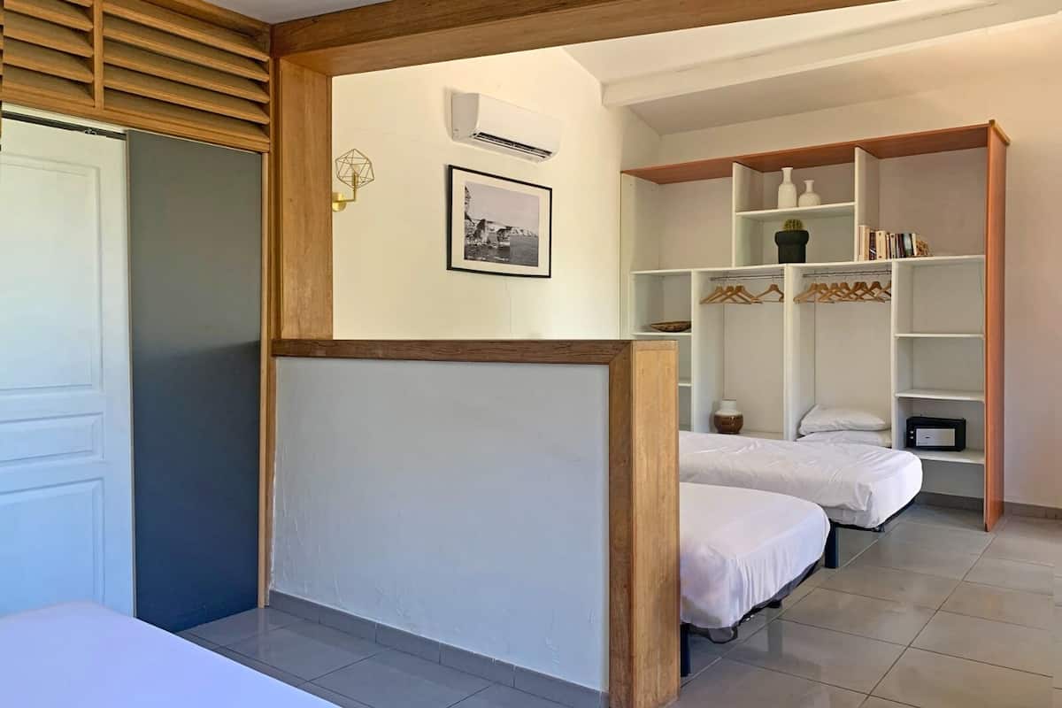 A hotel room with two beds, a white wardrobe, a small shelf with books and decorative items, and a framed picture on the wall.