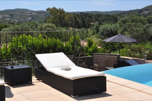 Zona de piscina con una silla de descanso, una mesita y una sombrilla.