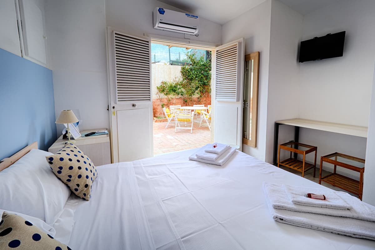 Une chambre d’hôtel équipée d’un lit, d’un bureau, d’une chaise, d’un climatiseur et offrant une vue sur la terrasse extérieure.