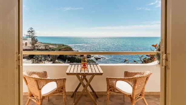 Un balcon doté de fauteuils et d’une table en osier, offrant une vue imprenable sur la côte, la mer et le paysage rocheux.