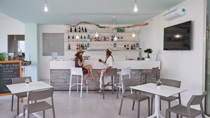Un espace bar moderne avec des chaises et des tables blanches, une variété de bouteilles exposées sur des étagères et un menu écrit à la craie.