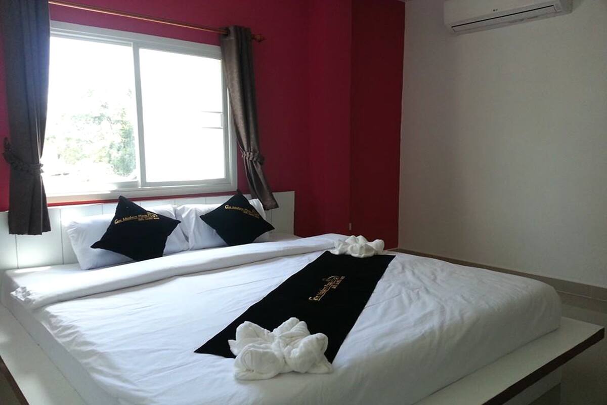 A hotel room with a bed, a window with curtains, and an air conditioning unit on the wall.