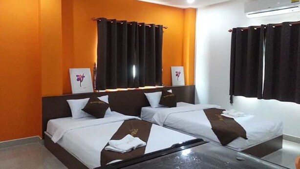 A hotel room with two beds, orange walls, and a large window with curtains. - GM Modern Place (Udon Thani)