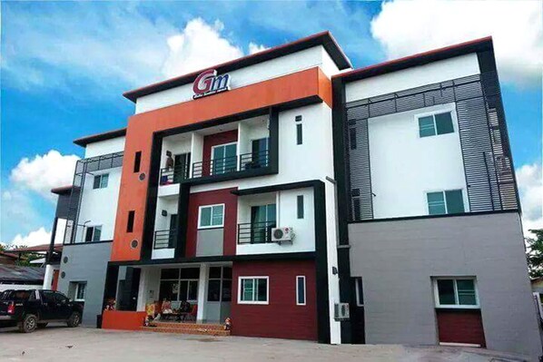 A multi-story building with a prominent 'Gm' sign, balconies, and a car parked in front. - GM Modern Place (Udon Thani)