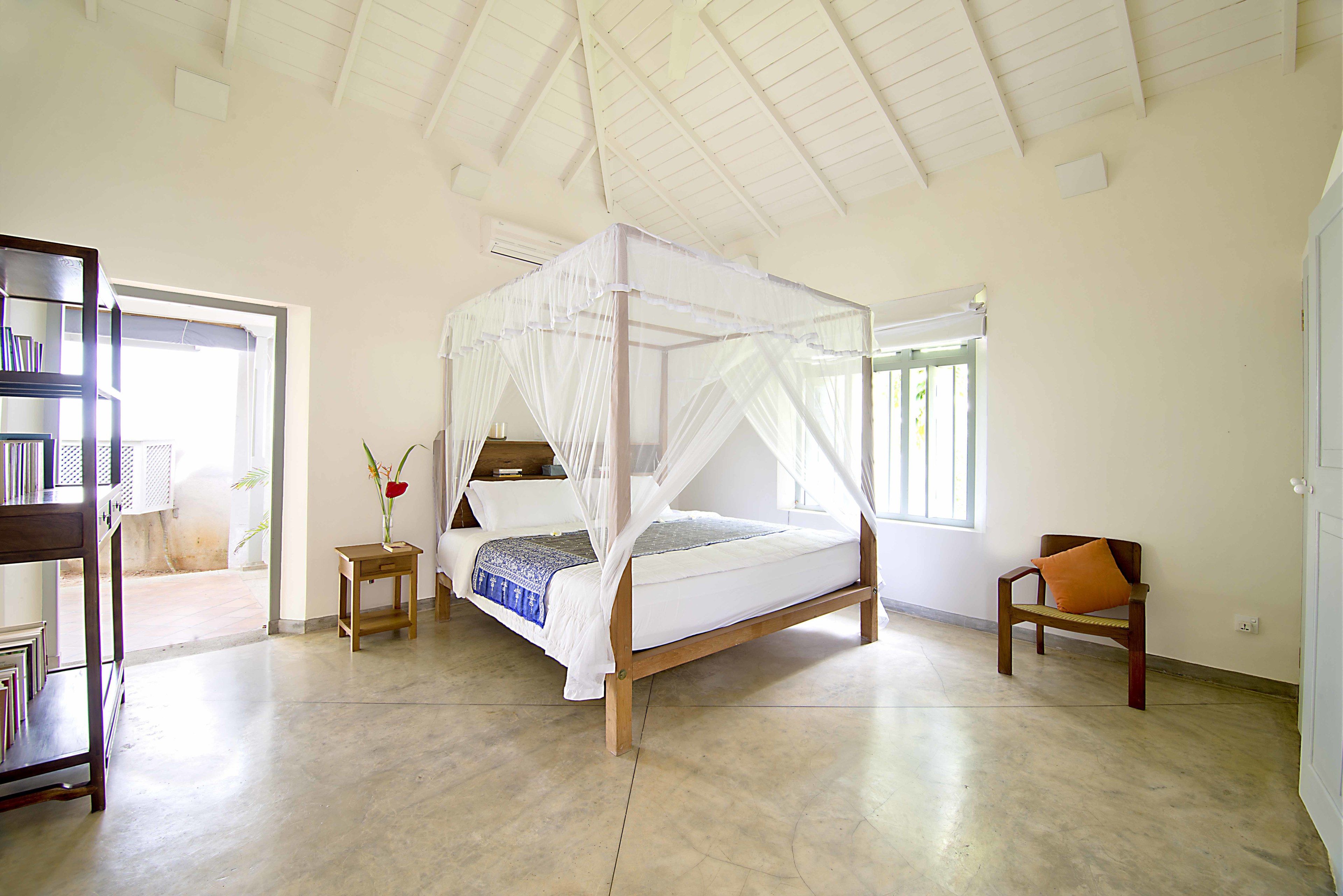 A spacious bedroom with a four-poster bed, a small bedside table, a chair, and a bookshelf.
