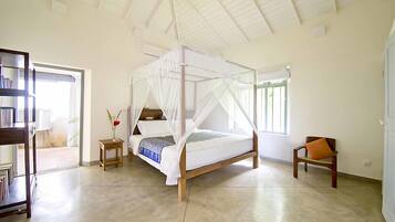 A spacious bedroom with a four-poster bed, a small bedside table, a chair, and a bookshelf.