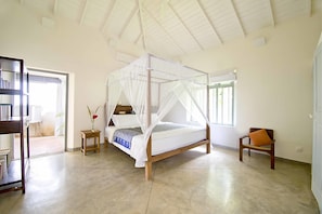 A spacious bedroom with a four-poster bed, a small bedside table, a chair, and a bookshelf. - Suriyawatta (Weligama)
