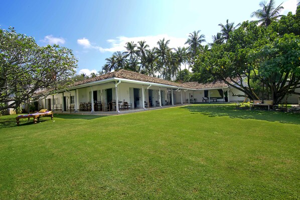 A hotel with a covered outdoor area, palm trees, and a well-maintained lawn. - Suriyawatta (Weligama)