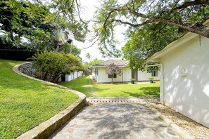 A stone pathway leading to a white building with a tiled roof, surrounded by lush greenery and a well-maintained lawn. - Suriyawatta (Weligama)