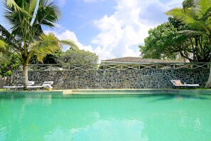 A clear pool with lounge chairs, palm trees, and a stone wall. - Suriyawatta (Weligama)