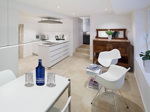 Una cocina moderna con armarios blancos, un comedor con mesa y sillas blancas, y un mueble de madera con espejo.