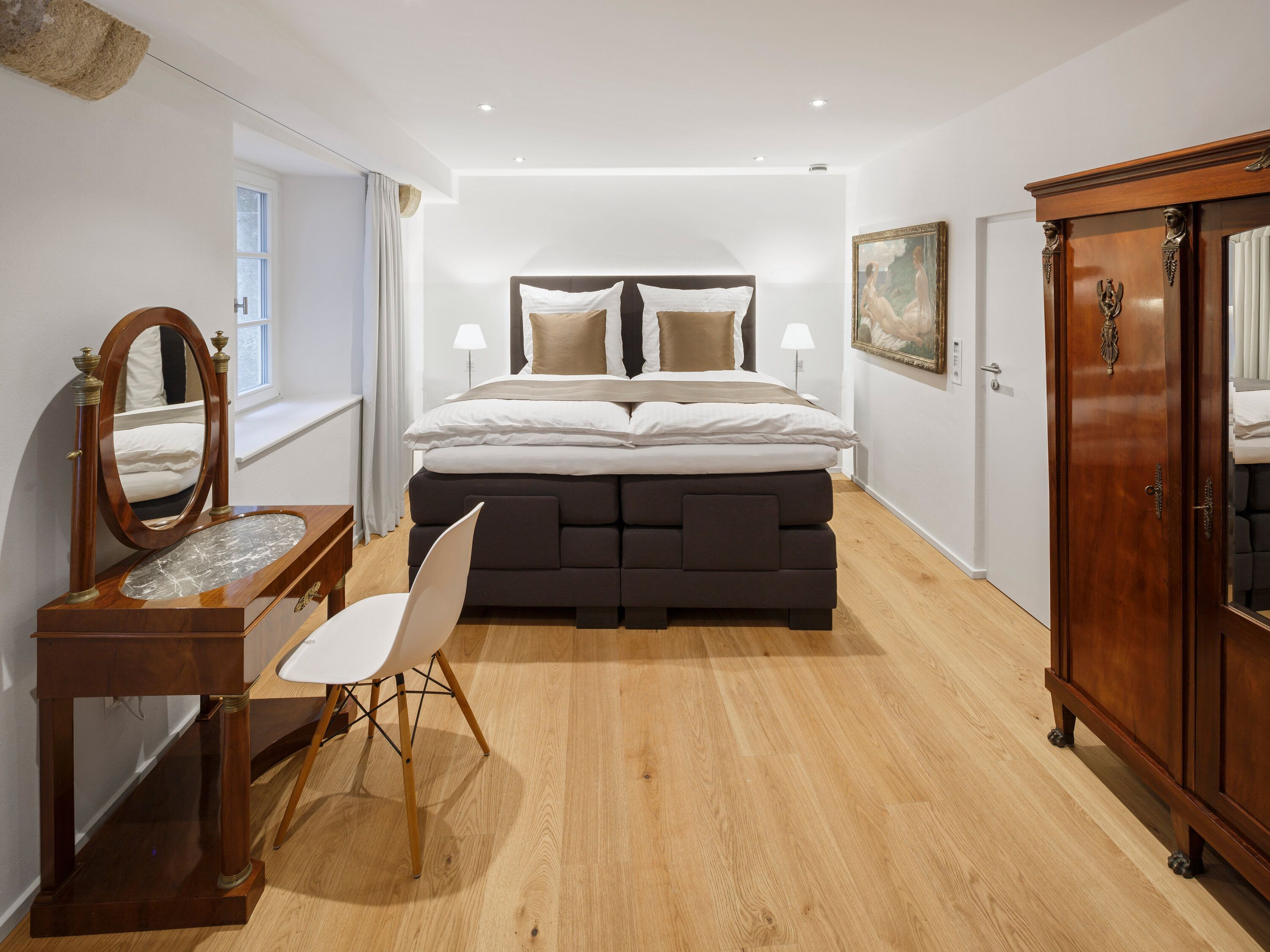 A bedroom with a large bed, a dresser, a vanity with a mirror, and a chair.