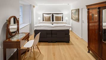 A bedroom with a large bed, a dresser, a vanity with a mirror, and a chair.